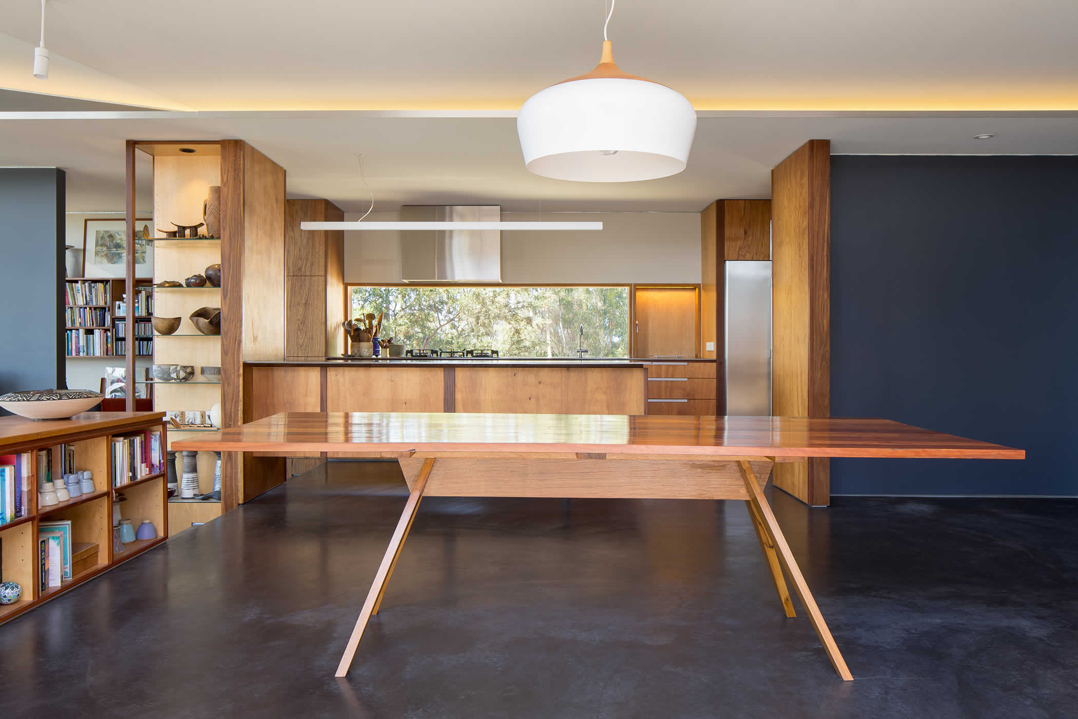 Sandy Bay, Tasmania: A horizontal kitchen window brings in natural light and forest views. Steel countertops, veneered timber plywood cabinetry and display shelving combine to complement the natural setting. Photo by Thomas Ryan.