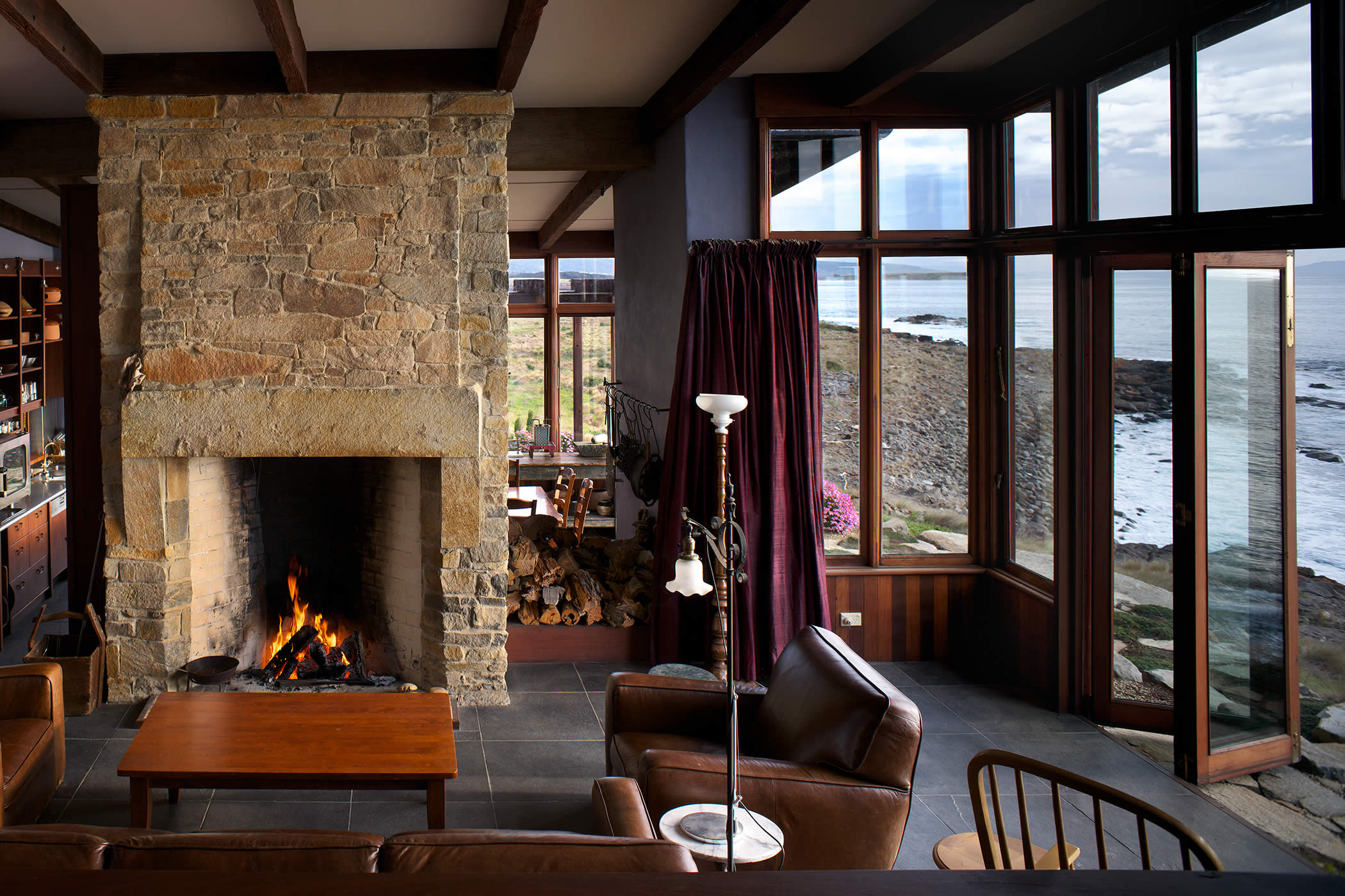 Thalia Haven, east coast Tasmania: The living room enjoys added ambience imbued by a beautiful, functional stone fireplace, though this environmentally sustainable luxury residence is fully off-the-grid. Photo by Ray Joyce.