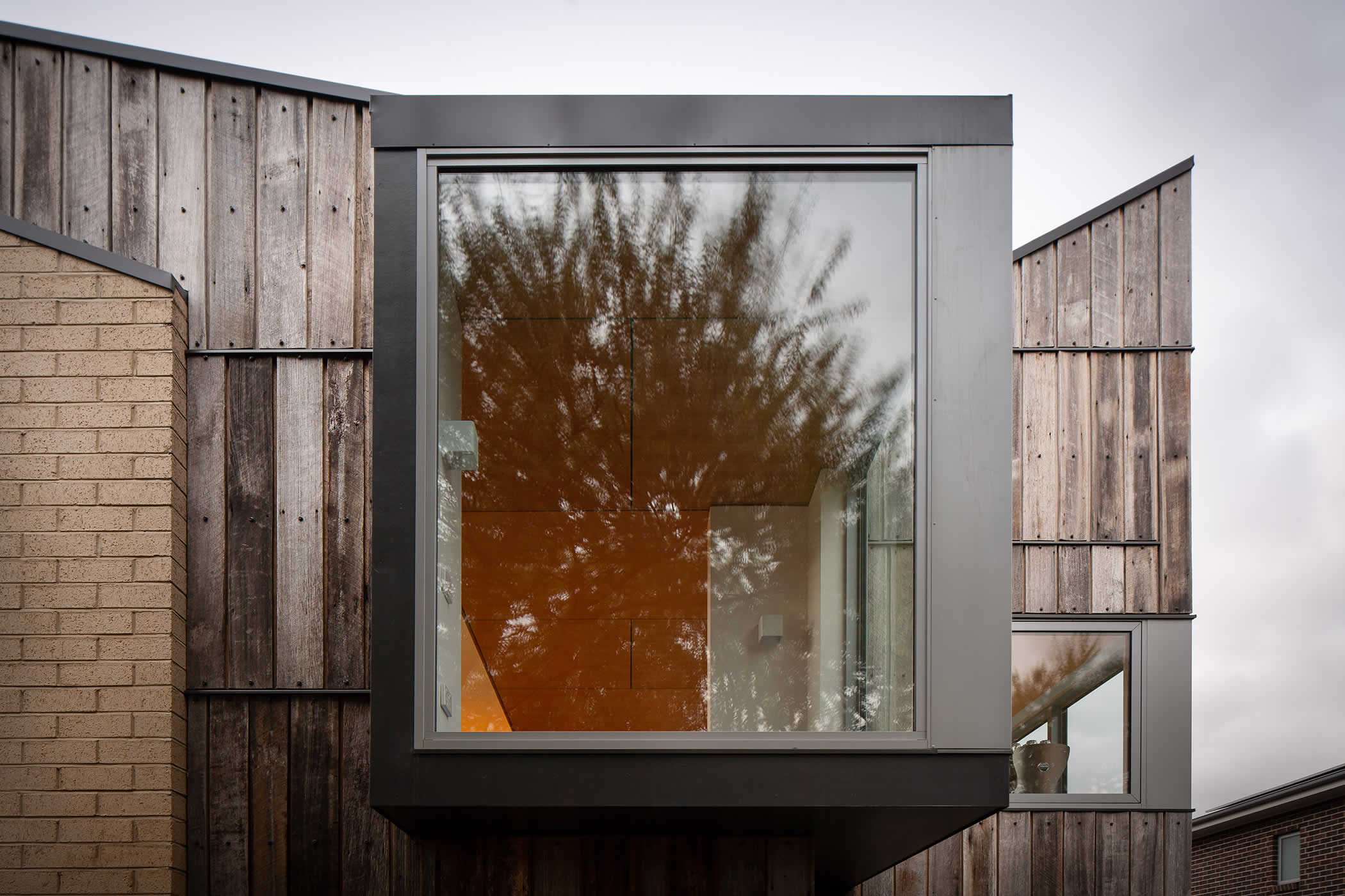 Tiger House, Lindesfarne, Tasmania: A corner alcove window, a clipped feature separately expressed, is clad in recycled, weathered, Tas Oak greys. Angular roof forms and light coloured brickwork create a lively contrast.  Photo by Thomas Ryan.