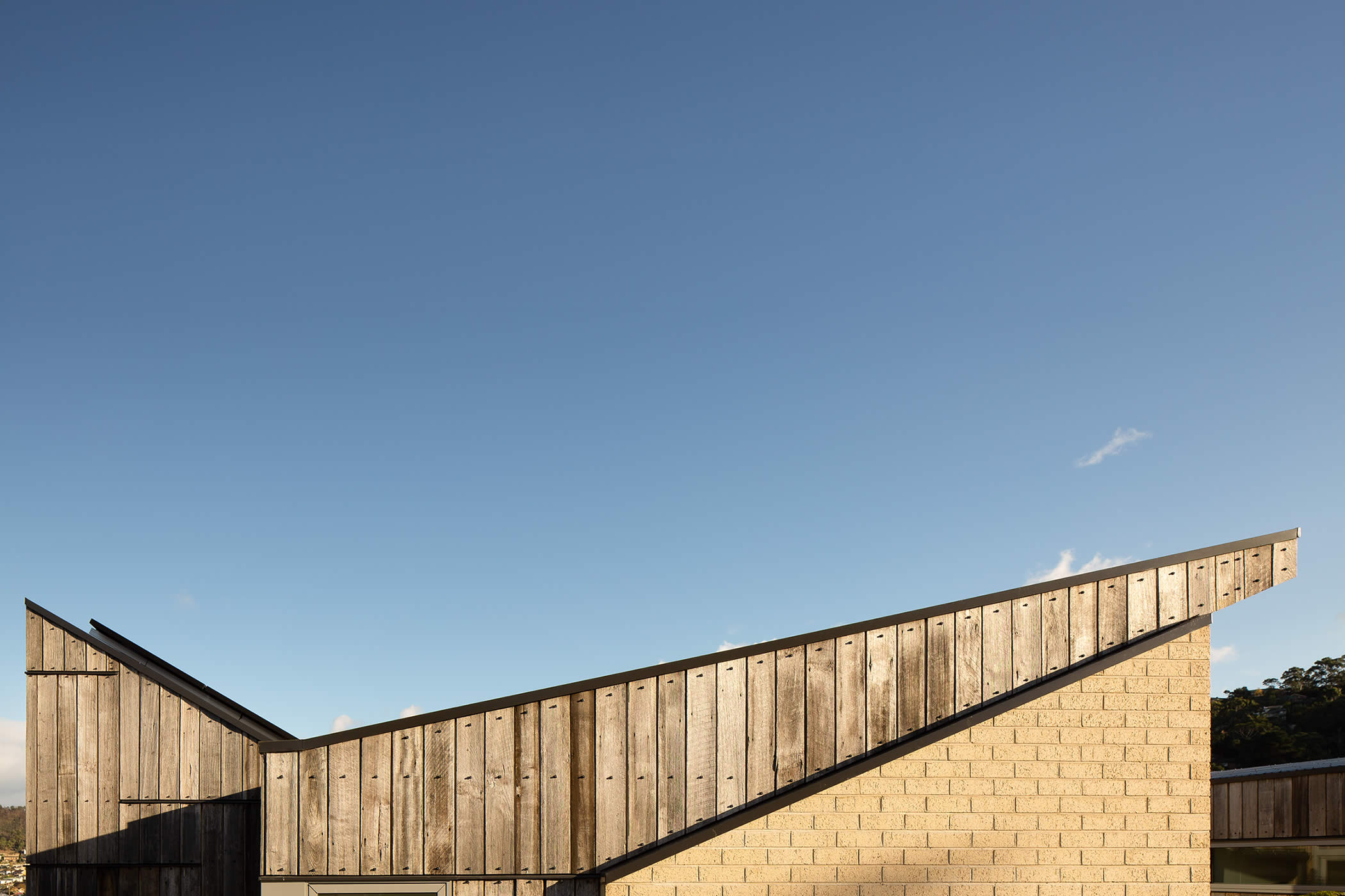 Tiger House, Lindesfarne, Tasmania: Angular roof forms maximize sunlight into living spaces and onto roof-mounted solar panels above the kitchen. They create a lively geometric play yet retain a modest scale that suits the home. Photo by Thomas Ryan.