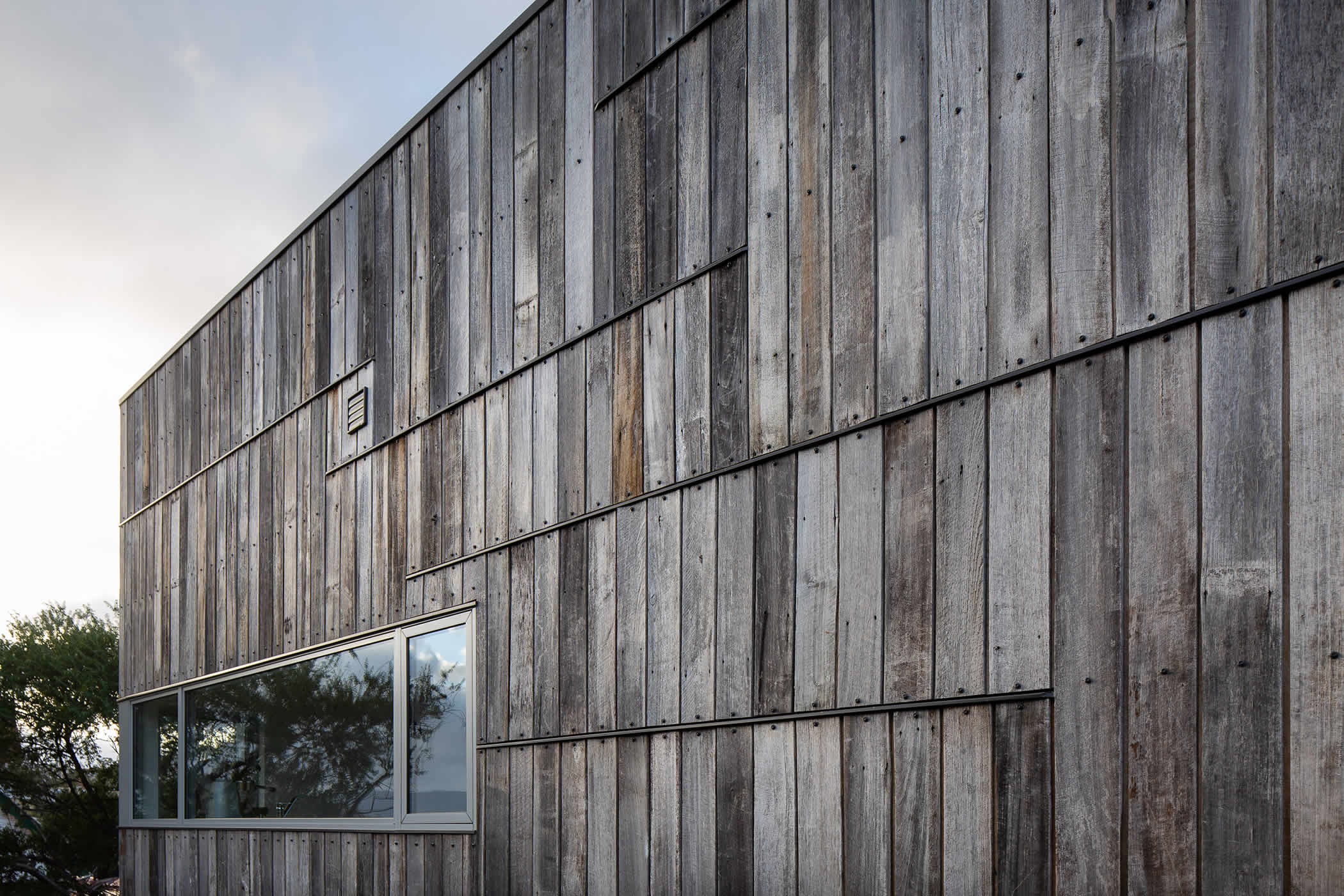 Tiger House, Lindesfarne, Tasmania: Scrap Tas Oak timber fence palings has been salvaged and re-used as external cladding. Weathered timber greys, varied cut down lengths and end capping, create a unique and memorable aesthetic. Photo by Thomas Ryan.