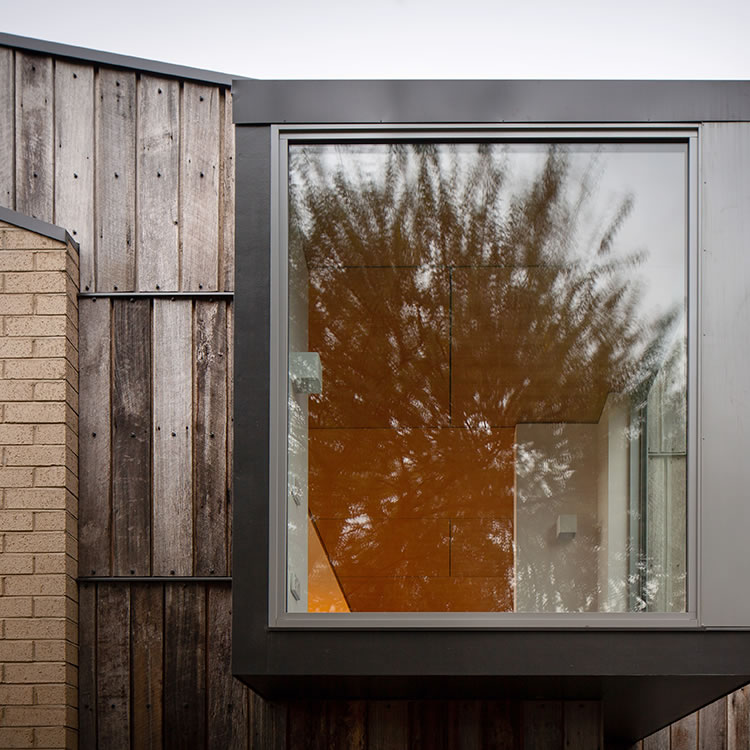 Tiger House, Lindesfarne, Tasmania: A corner alcove window, a clipped feature separately expressed, is clad in recycled, weathered, Tas Oak greys. Angular roof forms and light coloured brickwork create a lively contrast.