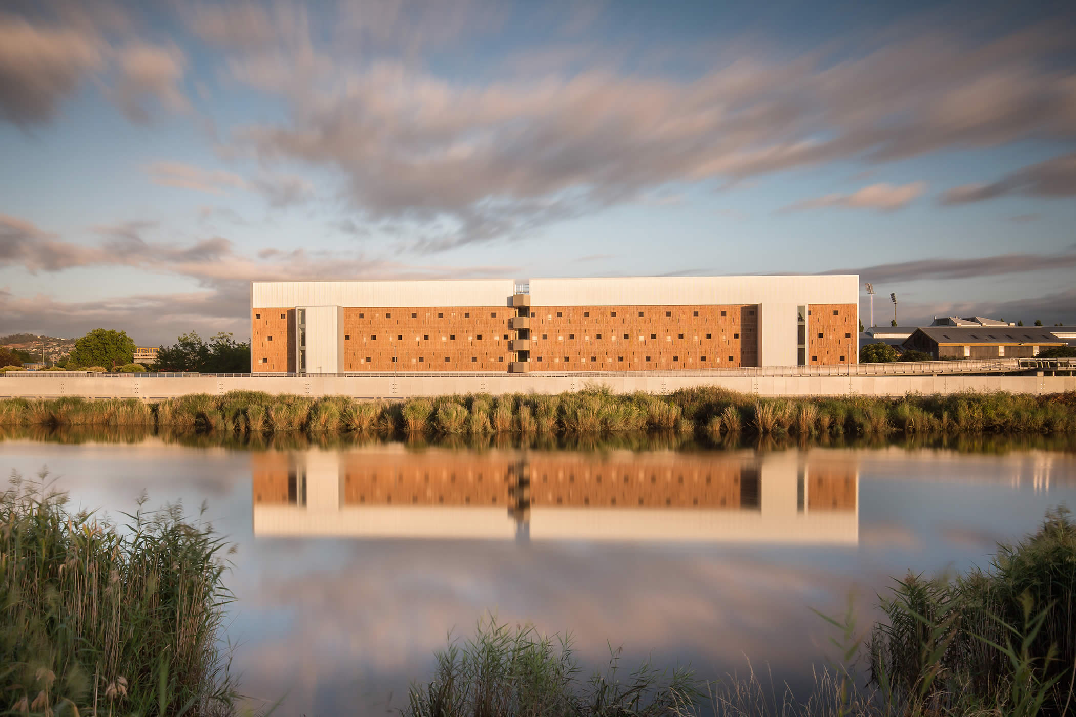 UTAS Inveresk Student Residences, Tasmania: Looking across the North Esk River to the building’s south facade and its reflection, raw macrocarpa timber screens evoke the adjacent delicate river foliage. Photo by Thomas Ryan.